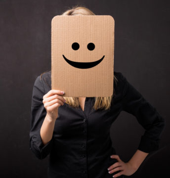 Woman holding a cardboard with smiley face in front of her face