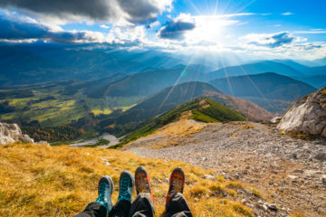 Two walkers sat looking out over mountains and countryside (you can only see their feet)