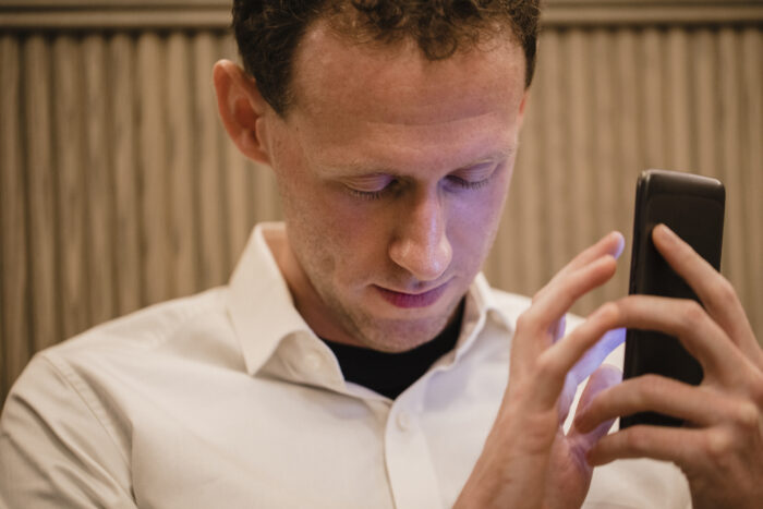 A close-up of a man wearing casual clothing, he has his smartphone in his hand and he is using a visually impaired mobile app to help assist him.