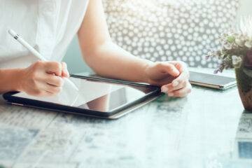 A person using a tablet with a pen at a table/ desk