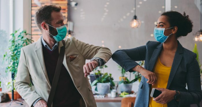 COVID19 Pandemic; Two colleagues wearing face masks touching elbows (instead of shaking hands) 