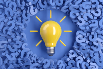 A yellow light bulb on background of blue question marksb