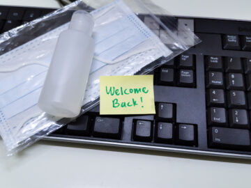 (alt="keyboard with a face mask, hand sanitizer and a welcome back note")