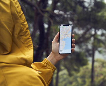(alt=”Person checking a map on a mobile phone in a forest setting