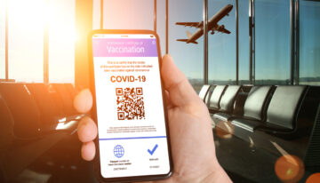 (alt=”Person holding a digital covid pass at the airport with a plane flying by a window”)
