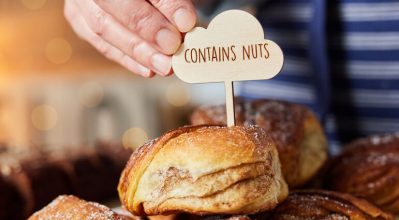 (alt=" person placing a sign "contains nuts" onto baked goods")