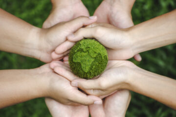 (alt=”Top view of hands holding the the earth on a green background. protect nature. Save Earth. concept of the environment ”)