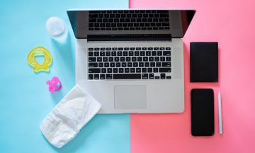 (alt="Laptop on a table; blue half with baby related items, pink half with work related items")