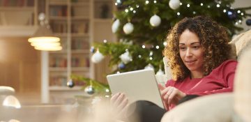 (alt="a lady sitting on a sofa, shopping on a tablet with a Christmas tree in the background”)