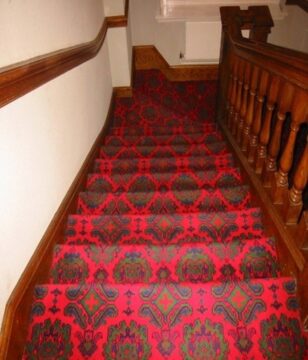(alt=”Stairs with a red patterned carpet, making it difficult to distinguish the beginning and end of the stairs”)